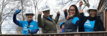 group of women volunteering at construction site, wearing safety equipment, lifting arms in poses