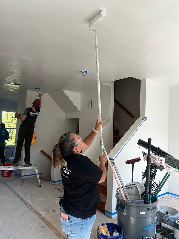 person painting ceiling with long stick paint roller