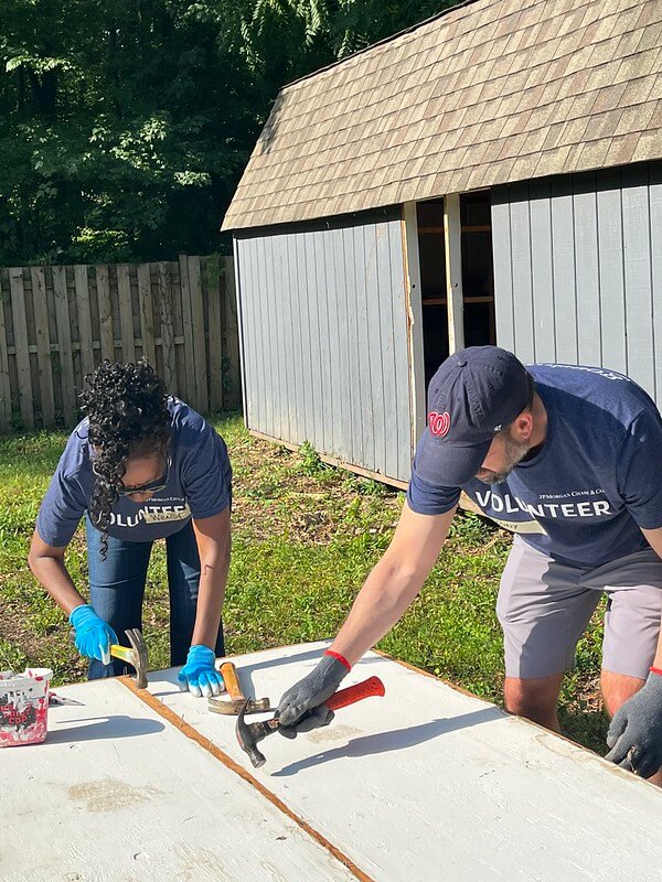 two people hammering nails on piece of wood