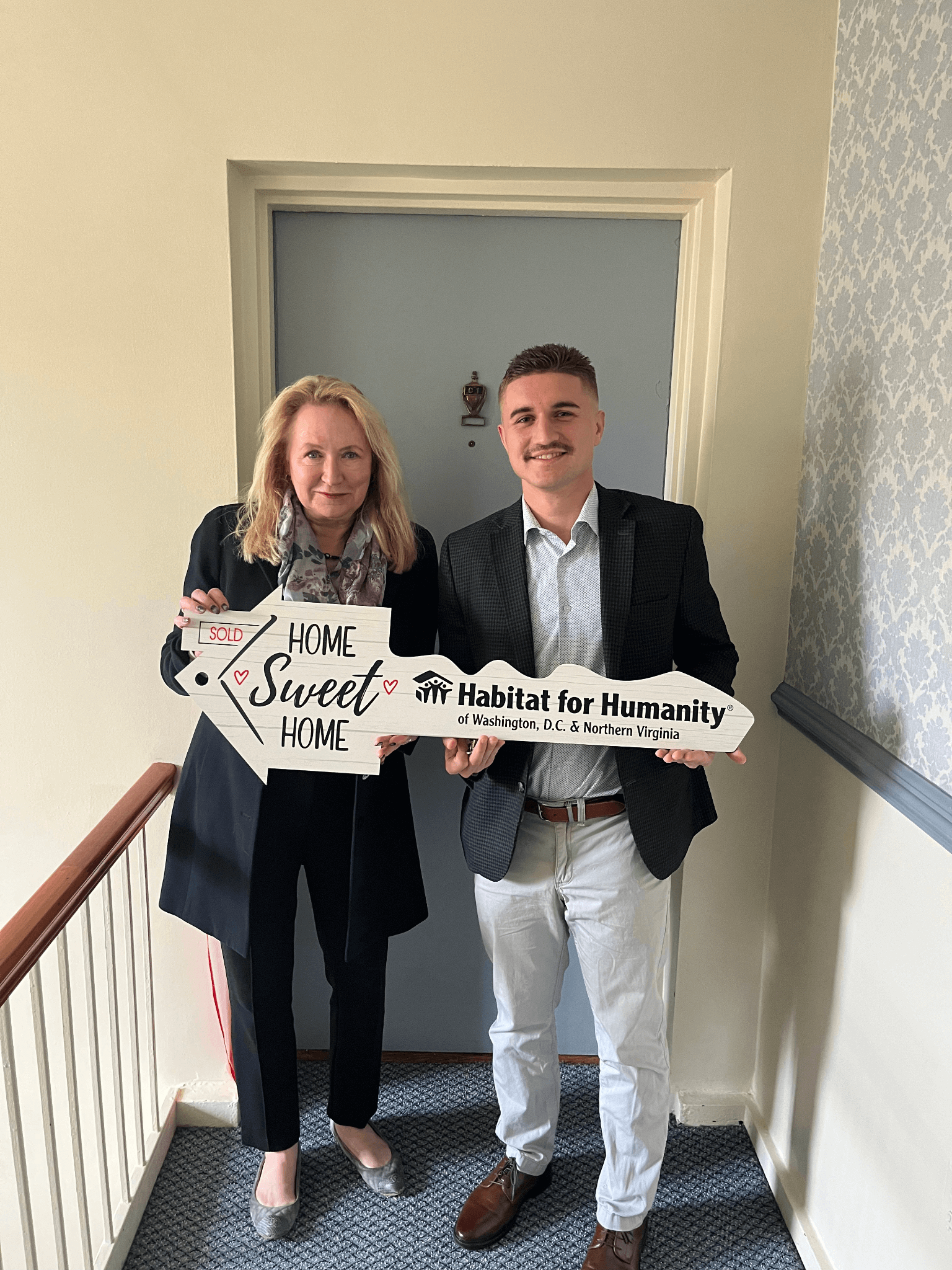 Susanne Slater, CEO of Habitat DC-NOVA with new homeowner, both holding large key-shaped cutout reading "home sweet home"